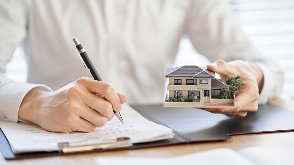Makelaar schrijft document terwijl zij een miniatuurwoning vasthoudt
